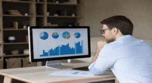 Gráficos financeiros e moedas com um smartphone exibindo "Orçamento Pessoal", representando a tecnologia simplificando o controle financeiro.